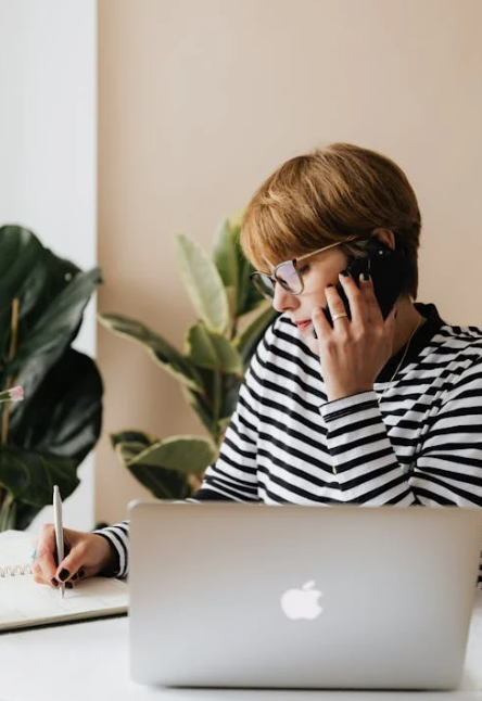 accueil femme au téléphone devant son ordinateur portable qui prend des notes