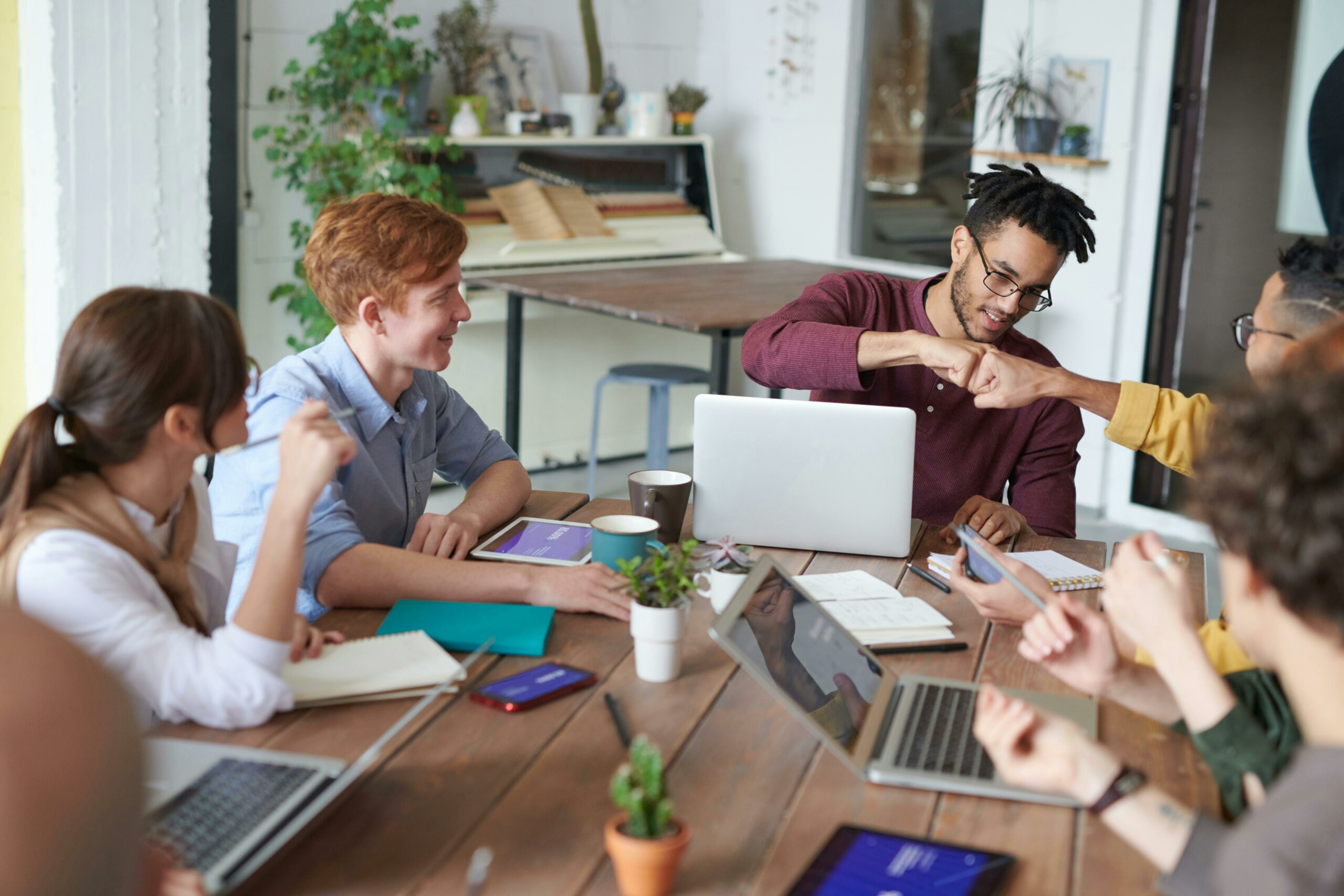 a propos - une équipe de 5 personnes sont au travail autour d'un bureau, 2 se checkent le poing